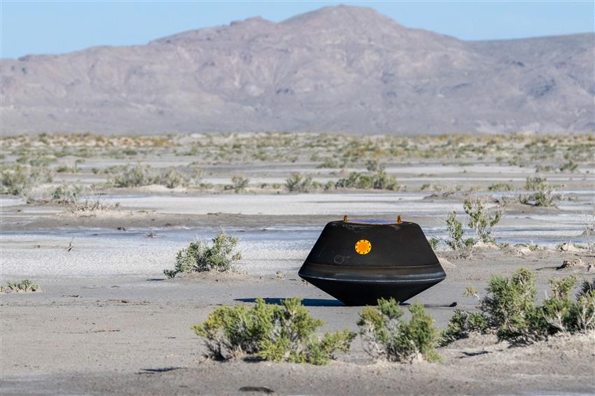 A black capsule in a desert; it is the sample return capsule from the OSIRIS-REx mission